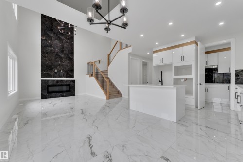 Spacious living area featuring polished marble-look flooring, a dramatic black-tiled fireplace wall with a linear electric fireplace, and a striking black chandelier - 12623 44 Street, Edmonton, AB 