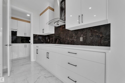 Kitchen featuring white flat-panel cabinetry, white countertops, dark stone backsplash, and stainless steel range hood - 12623 44 Street, Edmonton, AB 