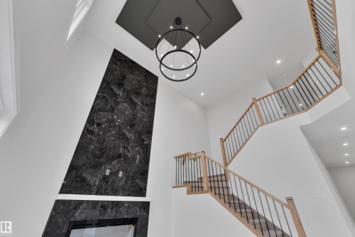 Two-story foyer featuring a striking dark marble-effect fireplace surround, a prominent contemporary chandelier, and a custom wood-finish staircase with black metal balusters - 12623 44 Street, Edmonton, AB 
