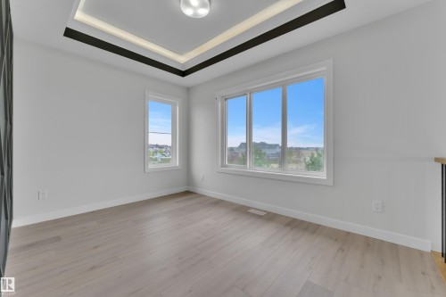 Spacious room featuring wood-finish flooring, multiple windows, a decorative tray ceiling with accent lighting, and a modern ceiling fixture - 12623 44 Street, Edmonton, AB 