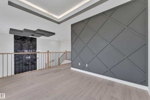 Open loft area showcasing a distinctive geometric accent wall, light wood-finish flooring, and a contemporary railing with wood newel posts and metal spindles - 12623 44 Street, Edmonton, AB 