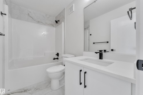 Contemporary bathroom featuring a white vanity with integrated sink, matte black fixtures, and a spacious bathtub with a tiled surround - 12623 44 Street, Edmonton, AB 