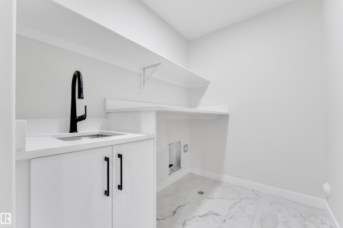 Utility room featuring a built-in sink with a matte black faucet, white cabinetry, and a light-toned countertop - 12623 44 Street, Edmonton, AB 
