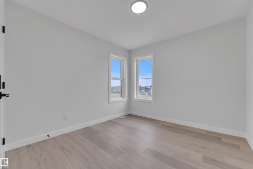 Light-filled interior space featuring two windows with white trim, wood-finish flooring, white baseboards, and a contemporary flush-mount ceiling light - 12623 44 Street, Edmonton, AB 