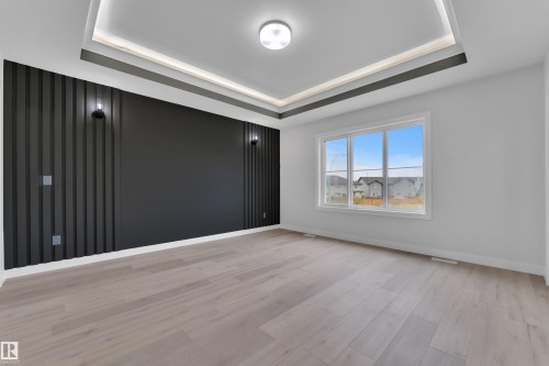 Spacious room featuring wood-finish flooring, a contemporary tray ceiling with recessed lighting, and a prominent accent wall with vertical slat detailing and two wall-mounted sconces - 12623 44 Street, Edmonton, AB 