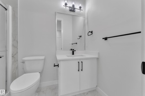 Bathroom featuring a white vanity with a single basin sink and black fixtures, a rectangular mirror, and a three-light vanity bar - 12623 44 Street, Edmonton, AB 