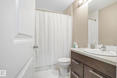 Full bathroom featuring a wood-finish vanity with a light countertop, an oval undermount sink, and a chrome faucet - 30 6075 Schonsee Way, Edmonton, AB - Indoor Photo Showing Bathroom