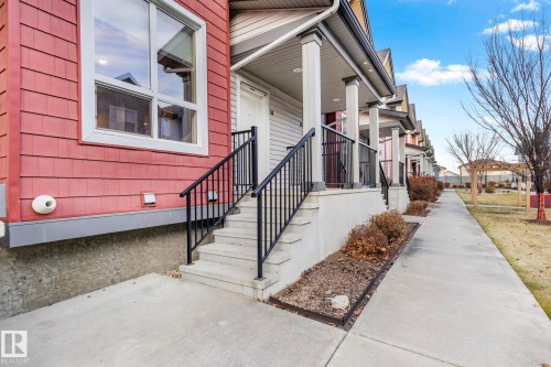 Exterior featuring red horizontal siding, concrete porch stairs with black metal railings, a white entry door, and a covered front porch with white columns - 30 6075 Schonsee Way, Edmonton, AB - Outdoor
