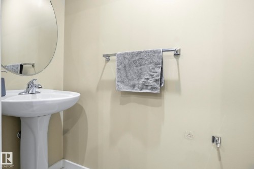 Pedestal sink with chrome faucet, complemented by a round wall-mounted mirror - 30 6075 Schonsee Way, Edmonton, AB - Indoor Photo Showing Bathroom