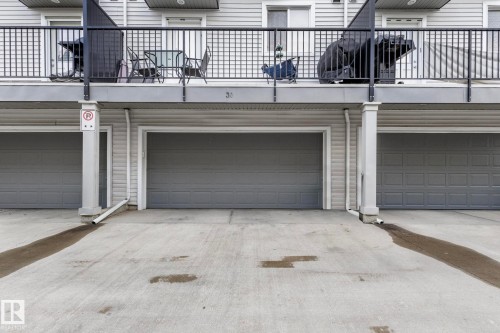 Three attached garages with panel doors, concrete driveway, and light gray siding exterior - 30 6075 Schonsee Way, Edmonton, AB - Outdoor With Exterior