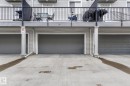 Three attached garages with panel doors, concrete driveway, and light gray siding exterior - 30 6075 Schonsee Way, Edmonton, AB  - Outdoor With Exterior 