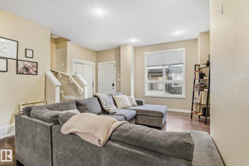 Living area featuring wood-finish flooring, light neutral paint, recessed lighting, white baseboards, and a large window with blinds - 30 6075 Schonsee Way, Edmonton, AB - Indoor Photo Showing Living Room