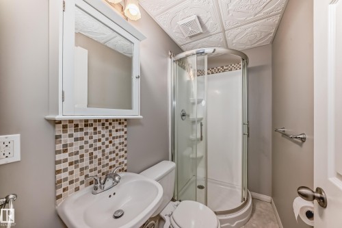 Bathroom featuring a curved glass shower enclosure, white wall-mounted vanity with a ceramic basin, mosaic tile backsplash, and decorative ceiling tiles - 2339 28B Ave Avenue, Edmonton, AB - Indoor Photo Showing Bathroom