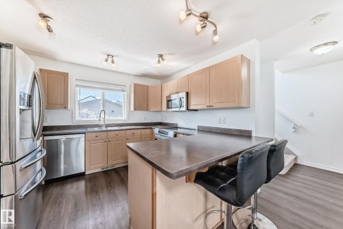 Kitchen featuring stainless steel appliances, light wood-finish cabinetry, a central island with a contrasting countertop, wood-finish flooring, and a window above the sink - 2339 28B Ave Avenue, Edmonton, AB - Indoor Photo Showing Kitchen
