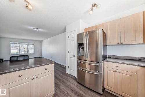 Stainless steel refrigerator with ice and water dispenser, light wood-finish cabinetry, dark countertop, wood-finish flooring, and track lighting fixture - 2339 28B Ave Avenue, Edmonton, AB - Indoor Photo Showing Kitchen