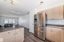 Stainless steel refrigerator with ice and water dispenser, light wood-finish cabinetry, dark countertop, wood-finish flooring, and track lighting fixture - 2339 28B Ave Avenue, Edmonton, AB  - Indoor Photo Showing Kitchen 
