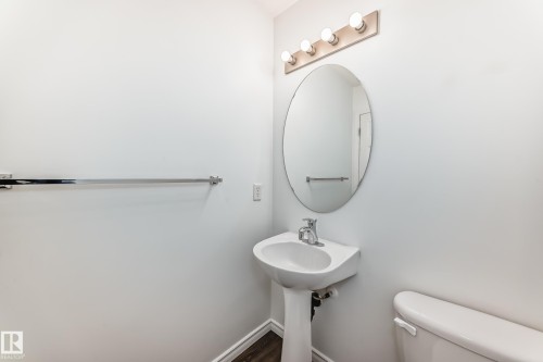 Pedestal sink with chrome faucet, an oval mirror, and a four-bulb vanity light fixture - 2339 28B Ave Avenue, Edmonton, AB - Indoor Photo Showing Bathroom