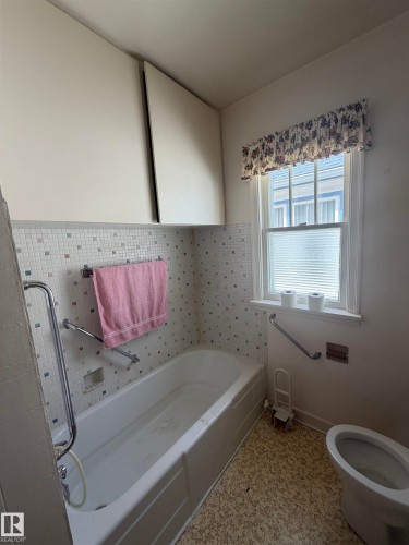 Bathroom featuring a built-in bathtub with subway tile surround, mosaic accent tiles, and two wall-mounted storage cabinets - 9630 106 Avenue, Edmonton, AB - Indoor Photo Showing Bathroom