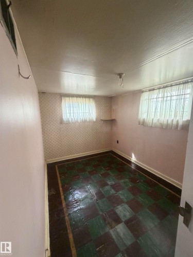Room featuring checkered floor tiles, two windows with white curtains, patterned wallpaper, and a wall-mounted shelf - 9630 106 Avenue, Edmonton, AB - Indoor Photo Showing Other Room