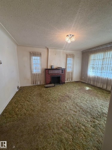 Living area featuring a brick fireplace surround, three windows, textured ceiling, and a flush-mount ceiling light fixture - 9630 106 Avenue, Edmonton, AB - Indoor Photo Showing Other Room