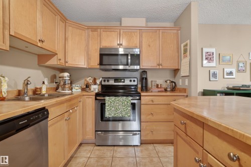 Kitchen featuring natural wood cabinetry, stainless steel appliances, a double basin sink, and wood-finish countertops - 110 2903 Rabbit Hill Road, Edmonton, AB - Indoor Photo Showing Kitchen With Double Sink