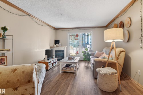 Living area featuring wood-finish flooring, a white mantel, and a sliding glass door - 110 2903 Rabbit Hill Road, Edmonton, AB - Indoor Photo Showing Living Room With Fireplace