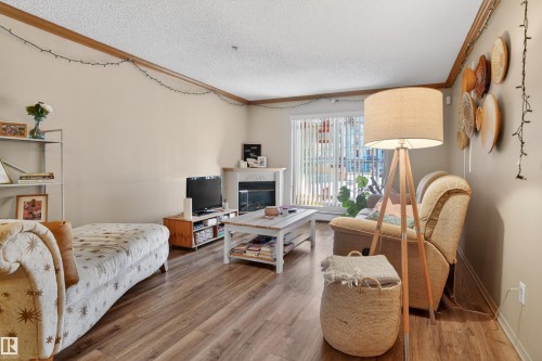 Living area featuring wood-finish flooring, a white-mantled fireplace, and a large sliding glass door - 110 2903 Rabbit Hill Road, Edmonton, AB - Indoor With Fireplace