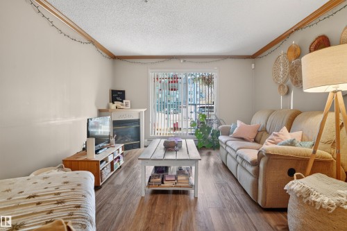 Living area with wood-finish flooring, a white mantelpiece, and a built-in fireplace - 110 2903 Rabbit Hill Road, Edmonton, AB - Indoor Photo Showing Living Room With Fireplace