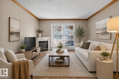 Living area featuring wood-finish flooring, a white mantel fireplace, and a sliding glass door - 110 2903 Rabbit Hill Road, Edmonton, AB - Indoor Photo Showing Living Room With Fireplace