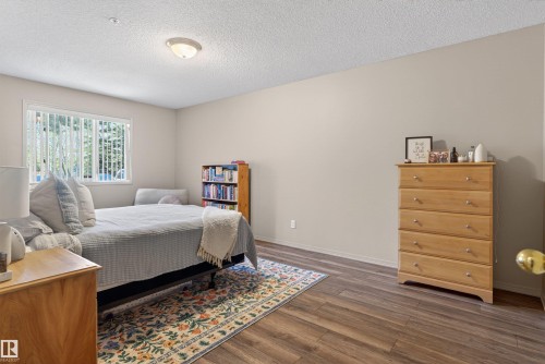 Spacious room featuring wood-finish flooring, a large window with vertical blinds, and neutral wall tones - 110 2903 Rabbit Hill Road, Edmonton, AB - Indoor Photo Showing Bedroom