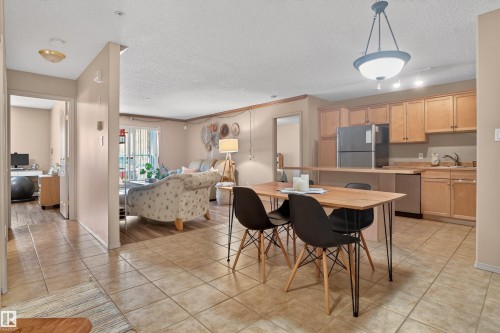 Kitchen and dining area featuring tile flooring, wood-finish cabinetry, a peninsula breakfast bar, and stainless steel appliances - 110 2903 Rabbit Hill Road, Edmonton, AB - Indoor