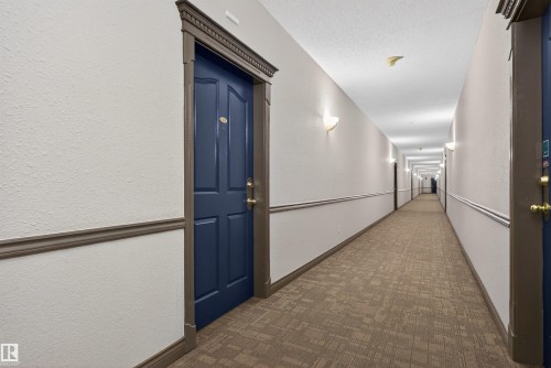 Hallway featuring a paneled door with decorative trim, textured walls, wall sconces, and patterned carpet flooring - 110 2903 Rabbit Hill Road, Edmonton, AB - Indoor Photo Showing Other Room