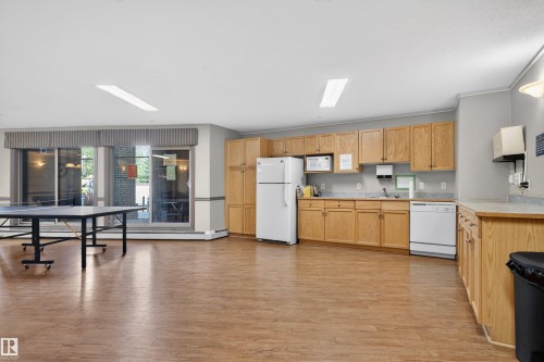Open-concept space featuring wood-finish flooring, a full kitchen area with light wood cabinetry and white appliances, and a large bank of sliding glass doors - 110 2903 Rabbit Hill Road, Edmonton, AB - Indoor Photo Showing Kitchen