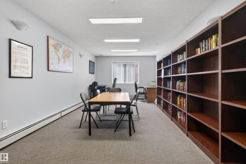 Room featuring extensive built-in shelving, light-toned carpeting, and multiple fluorescent ceiling lights - 110 2903 Rabbit Hill Road, Edmonton, AB - Indoor Photo Showing Office
