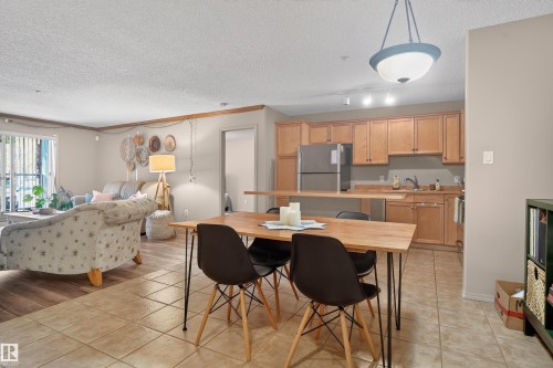 Open-concept living space featuring a dining area with tile flooring, a kitchen with light wood cabinetry and a stainless steel refrigerator, and a living area with wood-finish flooring - 110 2903 Rabbit Hill Road, Edmonton, AB - Indoor