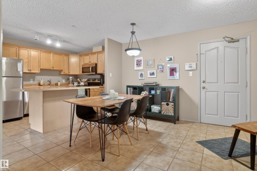 Open-concept living area with tile flooring throughout, featuring a kitchen with wood cabinetry and stainless steel appliances - 110 2903 Rabbit Hill Road, Edmonton, AB - Indoor