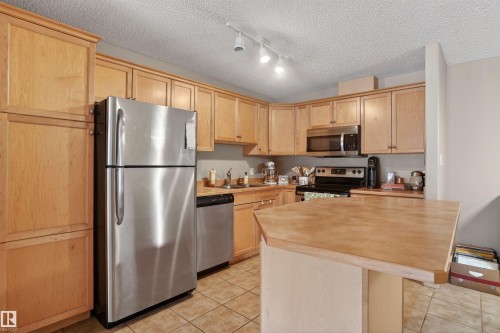 Kitchen featuring light wood cabinetry, stainless steel appliances, a built-in microwave, and tile flooring - 110 2903 Rabbit Hill Road, Edmonton, AB - Indoor Photo Showing Kitchen