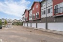 Multi-story townhomes with red and grey panel siding, individual garage doors, and private balconies with black railings - 3340 15A Avenue, Edmonton, AB  - Outdoor 