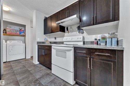 Kitchen featuring dark brown cabinets, white range with electric stovetop, under cabinet range hood, light countertops, and a textured ceiling - 6152 13 Avenue, Edmonton, AB - Indoor