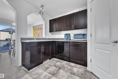 Kitchen with dark brown cabinets, black dishwasher, stainless steel microwave, a textured ceiling, and light tile patterned floors - 6152 13 Avenue, Edmonton, AB - Indoor Photo Showing Kitchen