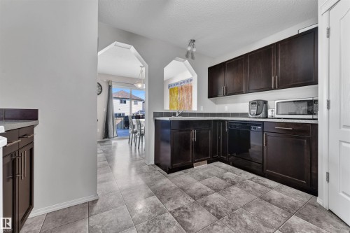 Kitchen featuring dark brown cabinetry, arched walkways, a textured ceiling, dishwasher, and light countertops - 6152 13 Avenue, Edmonton, AB - Indoor Photo Showing Kitchen