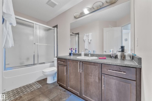 Bathroom featuring vanity, dark tile patterned flooring, bath / shower combo with glass door, and a textured ceiling - 6152 13 Avenue, Edmonton, AB - Indoor Photo Showing Bathroom