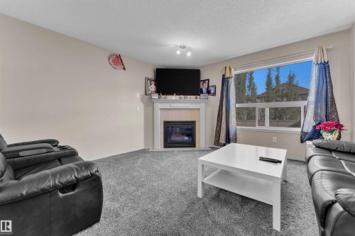 Living area with carpet flooring, a tile fireplace, and a textured ceiling - 6152 13 Avenue, Edmonton, AB - Indoor Photo Showing Living Room With Fireplace