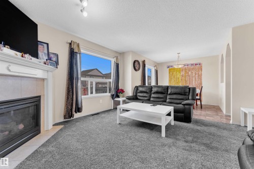 Living room with light colored carpet, a textured ceiling, light tile patterned floors, a tile fireplace, and arched walkways - 6152 13 Avenue, Edmonton, AB - Indoor Photo Showing Living Room With Fireplace