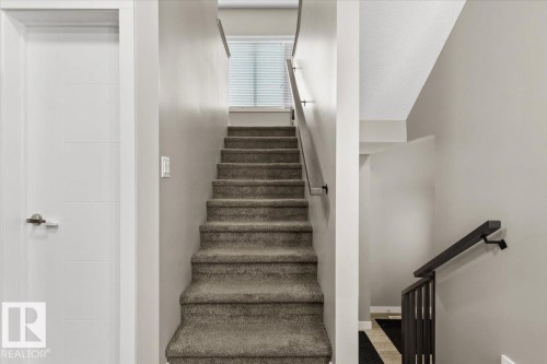 Carpeted staircase featuring a window with blinds, a modern white door with horizontal paneling, and dark handrails - 236 39 Avenue, Edmonton, AB - Indoor Photo Showing Other Room