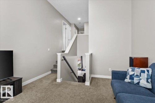 Carpeted living area featuring light gray walls, white trim, and a staircase with white balusters and a dark handrail - 236 39 Avenue, Edmonton, AB - Indoor
