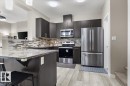 Modern kitchen featuring dark wood-finish cabinetry, stainless steel appliances, a grey patterned tile backsplash, a kitchen island with stone-finish countertop, and light wood-finish flooring - 236 39 Avenue, Edmonton, AB  - Indoor Photo Showing Kitchen With Upgraded Kitchen 