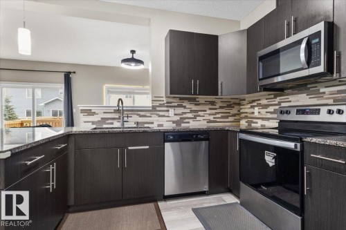 Contemporary kitchen featuring dark wood-finish cabinetry, granite-style countertops, stainless steel appliances, a mosaic tile backsplash, and a pass-through opening - 236 39 Avenue, Edmonton, AB - Indoor Photo Showing Kitchen With Upgraded Kitchen
