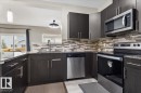 Contemporary kitchen featuring dark wood-finish cabinetry, granite-style countertops, stainless steel appliances, a mosaic tile backsplash, and a pass-through opening - 236 39 Avenue, Edmonton, AB  - Indoor Photo Showing Kitchen With Upgraded Kitchen 