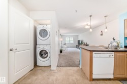 Integrated kitchen and living area featuring a stacked washer and dryer unit, tiled flooring, wood-finish cabinetry, and pendant lighting - 